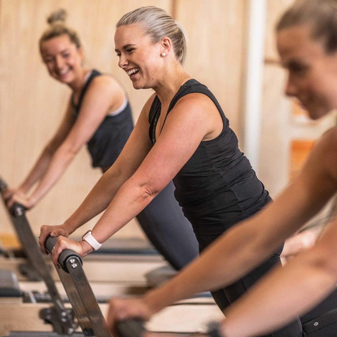 Woman on reformer laughing, blurred woman in background smiles